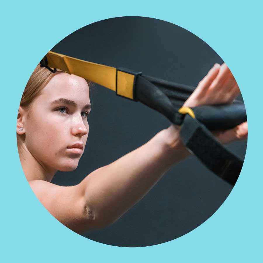 Eine Frau schaut fokussiert auf ihr TRX auf Höhe der Schultern.