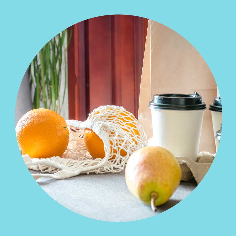 Im Obstnetz liegen zwei Manderinen auf dem Tisch. Davor eine Birne und dahinter zwei to got Kaffeebecher